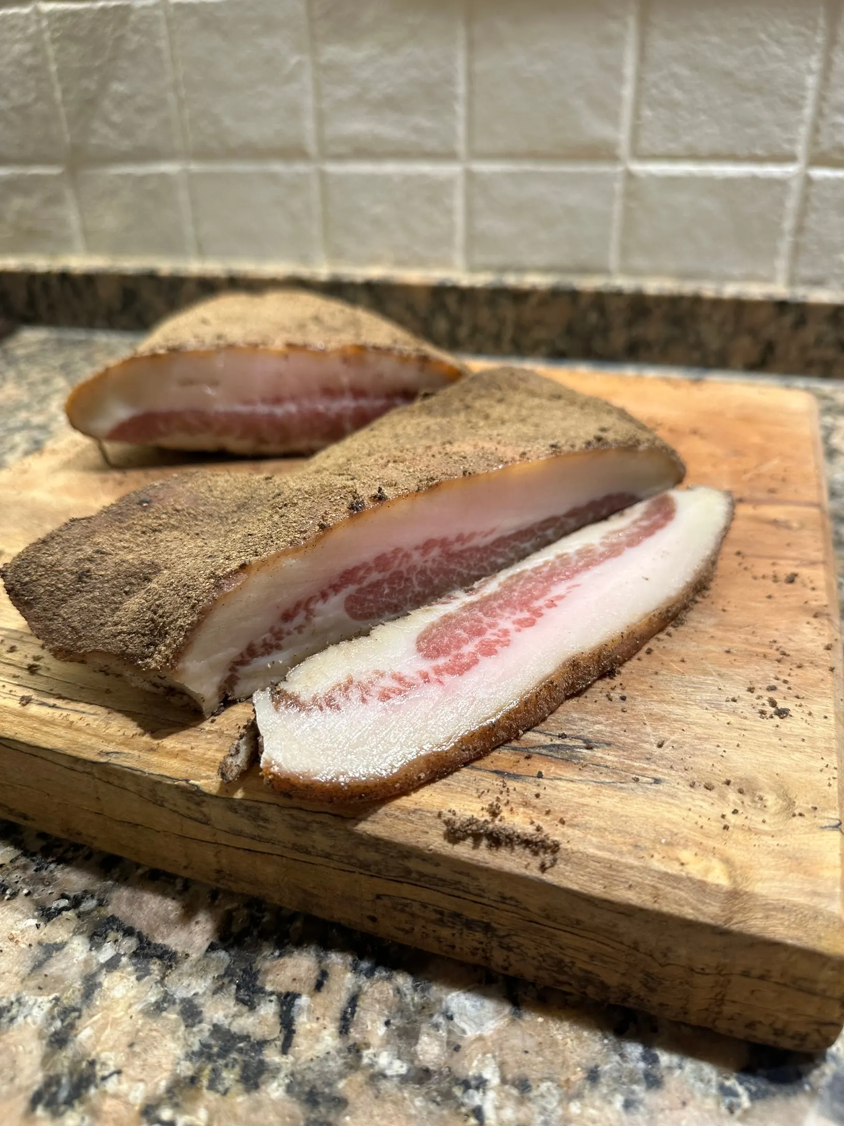 Pieza de guanciale artesanal cortada sobre tabla, con la corteza de pimienta y la grasa infiltrada a la vista