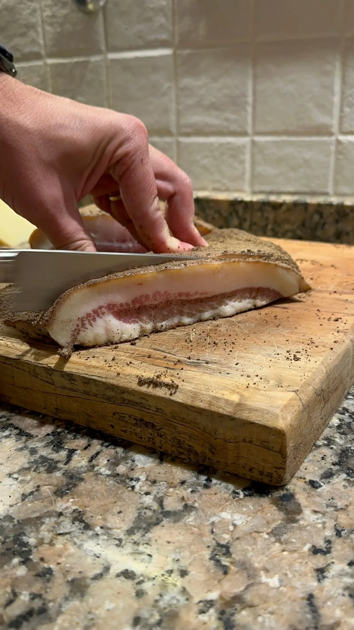 Pieza de guanciale ya curada, cortándose sobre una tabla de madera